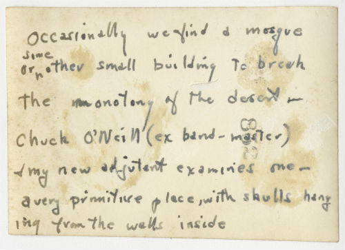 Charles "Chuck" O'Neill in front of a small building in the desert. Verso